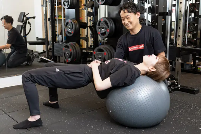 バランスボールのトレーニングを受ける女性とトレーナーの写真